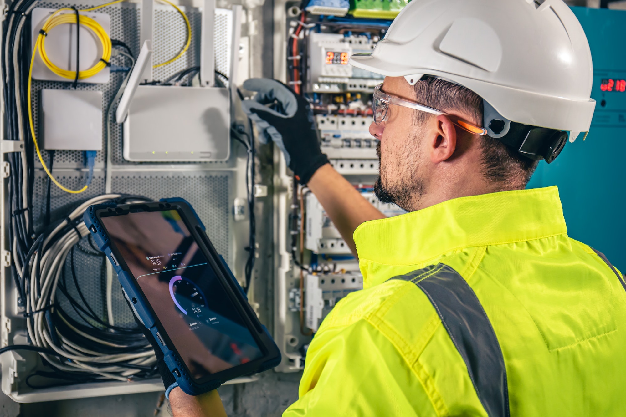 Man, an electrical technician working in a switchboard with fuses, uses a tablet.